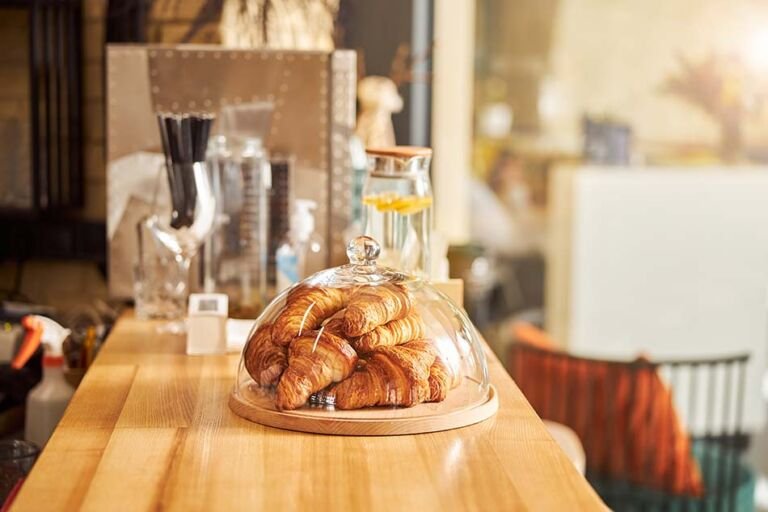 Wooden bar counter with a pile of croissants under a glass lid